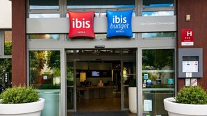 A hotel entrance with two signs for 'ibis Hotels' and 'ibis Budget Hotels,' a reception desk, and large potted plants. - Ibis Budget Dijon Centre Clemenceau (Dijon)