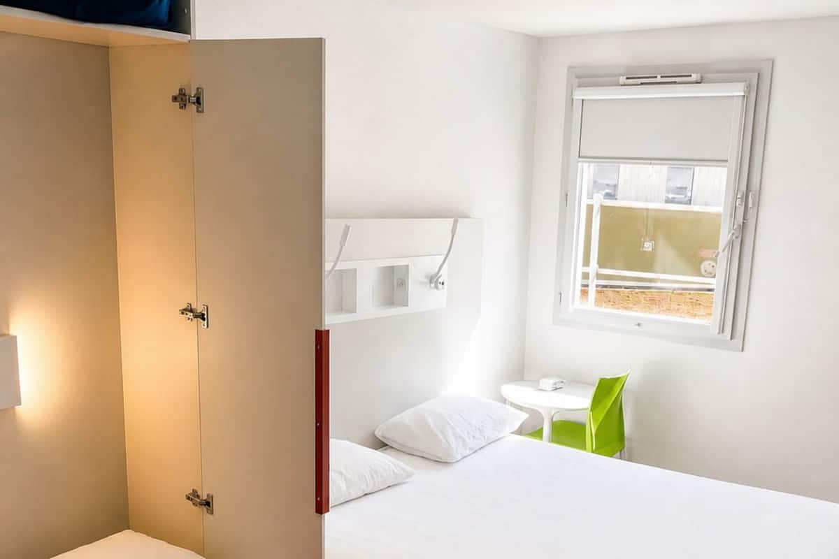 Een hotelkamer met twee bedden, een garderobe, een tafeltje en een raam.