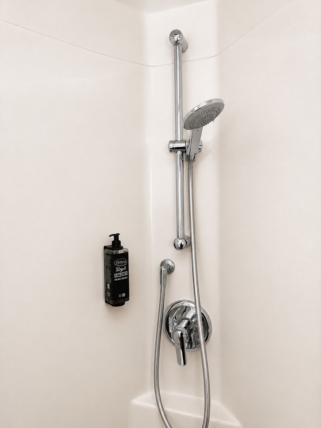 Ducha con cabezal de ducha de mano, grifo empotrado en la pared y dispensador de jabón manual.