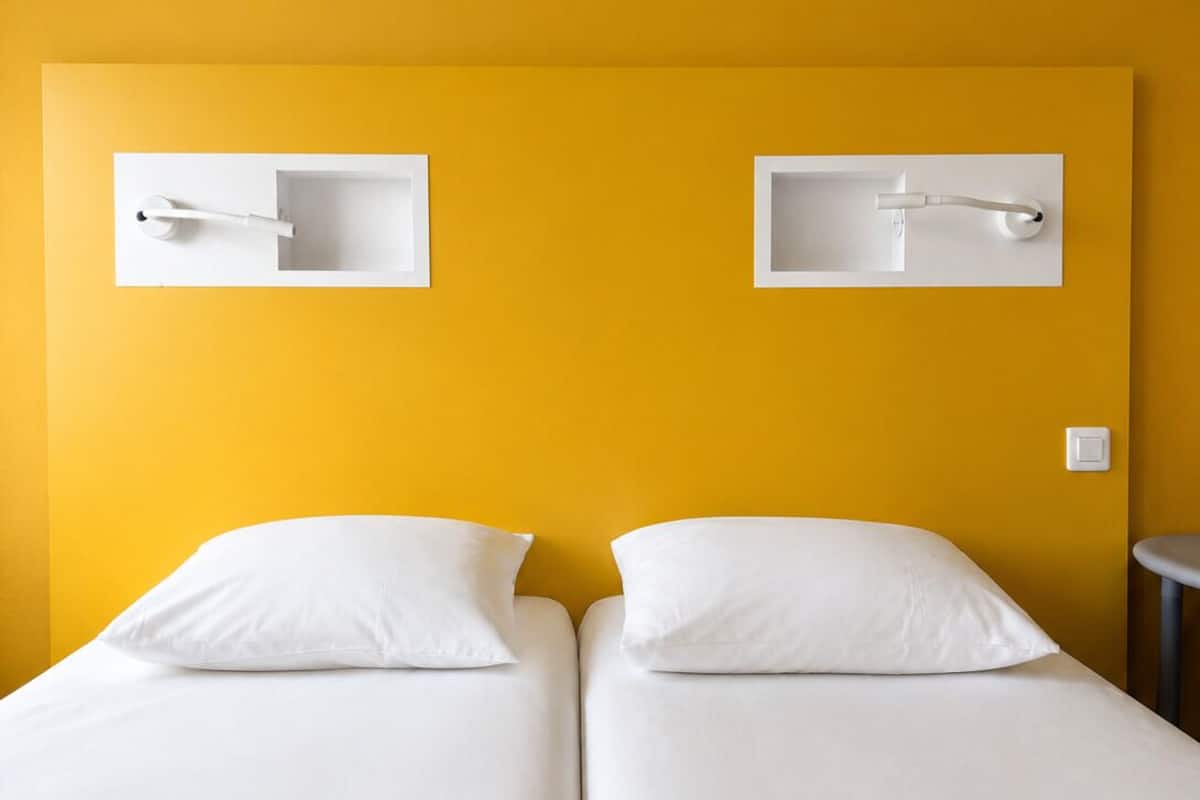 Een tweepersoonsbed met witte lakens, twee handdoekdispensers aan de muur en een klein rond tafeltje.