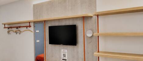 Una habitación moderna con un televisor de pared, estantes de madera y un perchero.