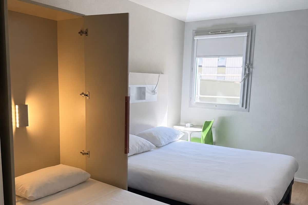 Een slaapkamer met twee bedden, een raam en een groene stoel.