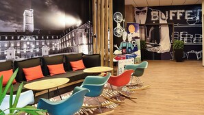 A modern lounge with a cityscape mural, comfortable seating, and a 'BUFFET' sign. - Ibis Budget Dijon Centre Clemenceau (Dijon)