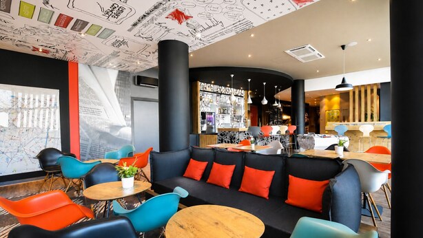 A modern interior with a black sofa, colorful chairs, a bar area, and a large map on the wall. - Ibis Budget Dijon Centre Clemenceau (Dijon)