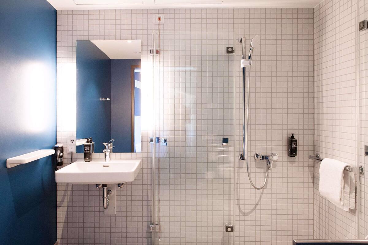 A modern bathroom with a glass-enclosed shower, a white sink with a mirror, and a towel rack.