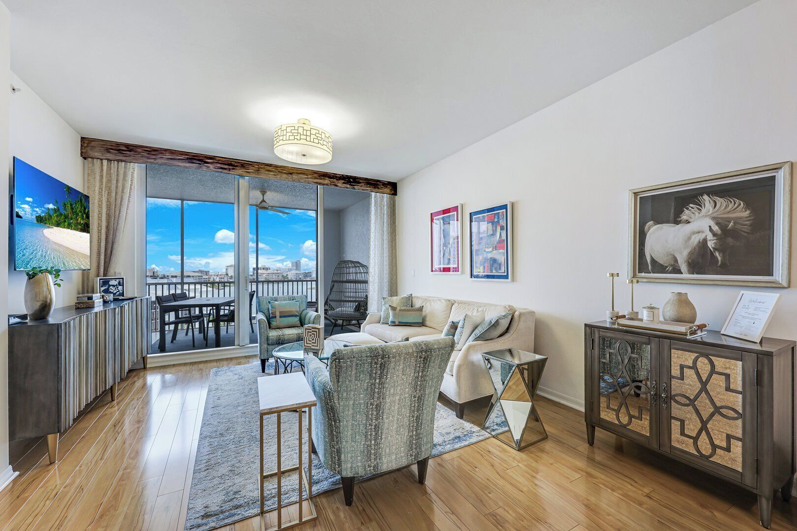 A spacious living room with a balcony, a sofa set, a dining area, and a cabinet with decorative items.