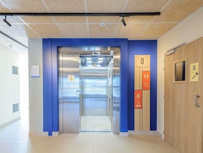 An elevator with a blue wall on one side and a wooden door on the other, leading to a tiled floor.