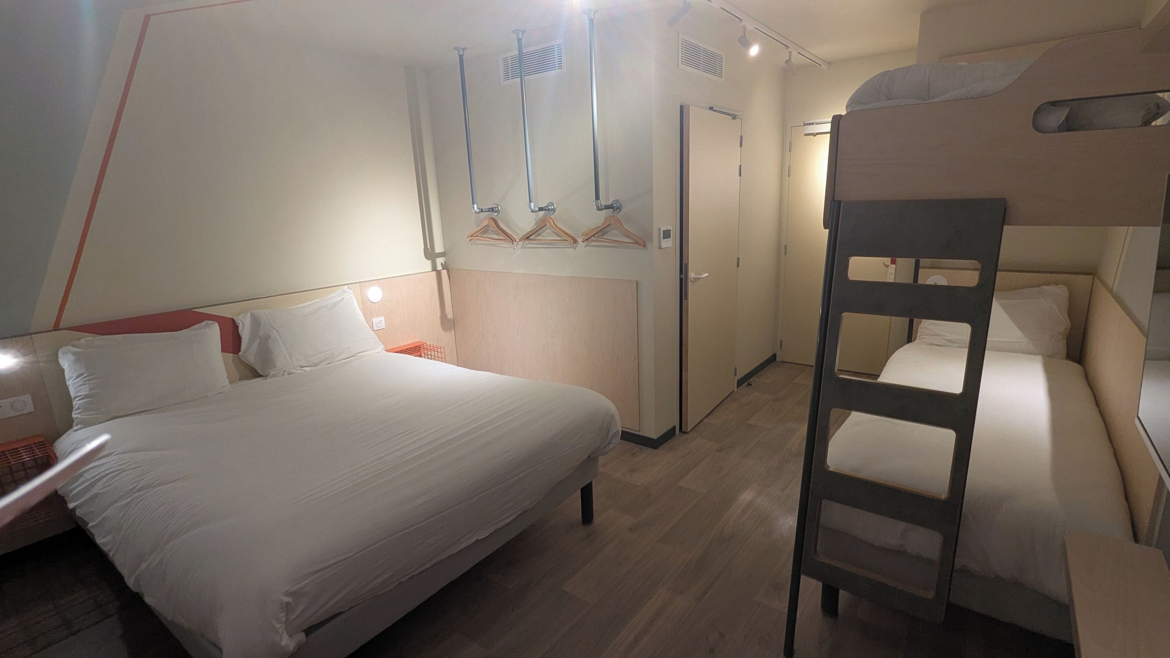 Habitación de hotel con literas, una cama individual, una mesita de noche, un armario y un espejo.