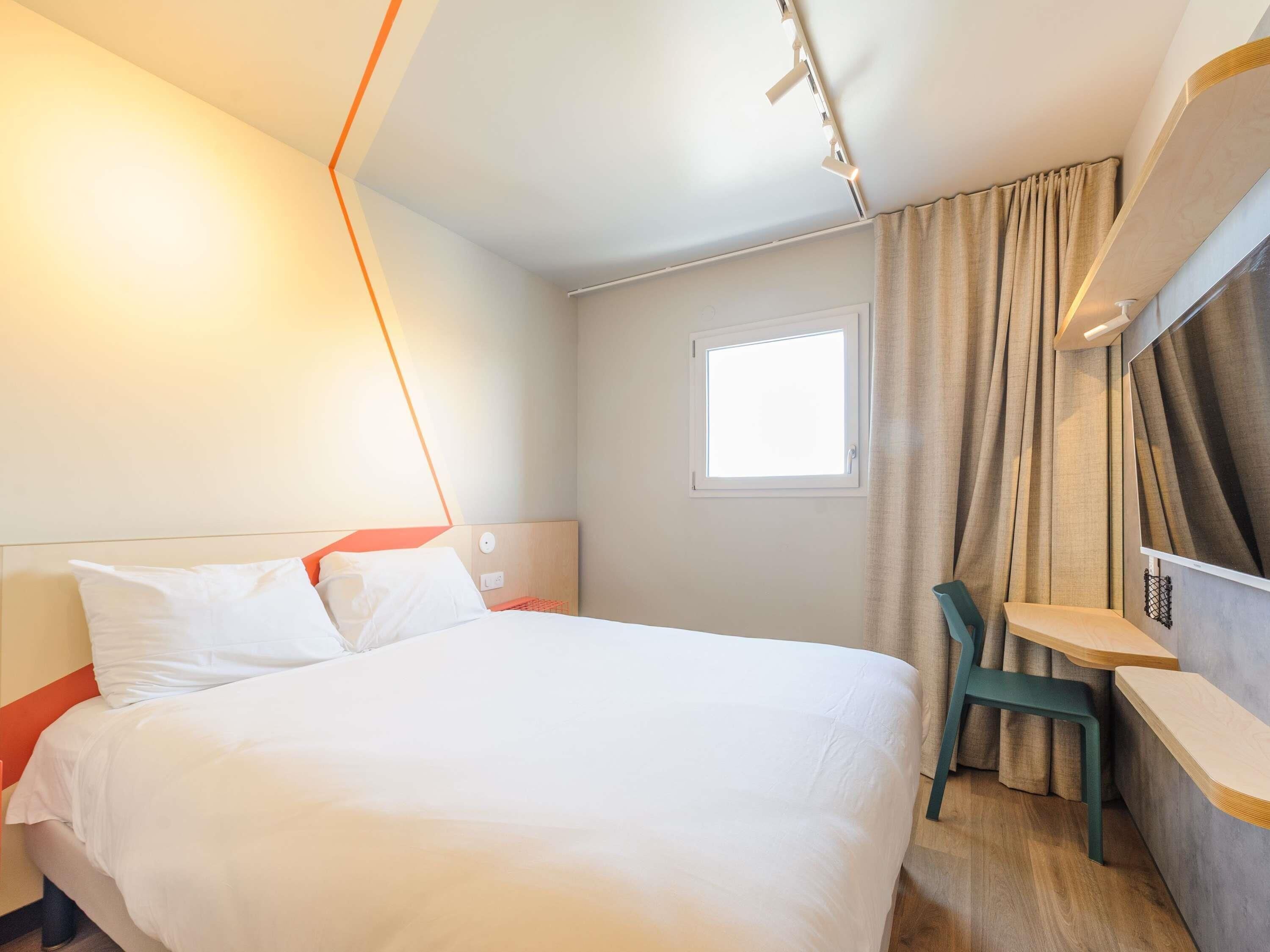 Ett hotellrum med en säng, ett skrivbord, en stol, ett fönster och en gardin.