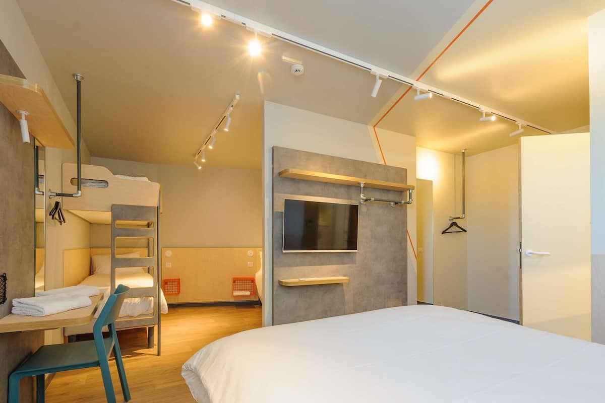 A modern hotel room with bunk beds, a desk, a chair, a TV, and a wardrobe.