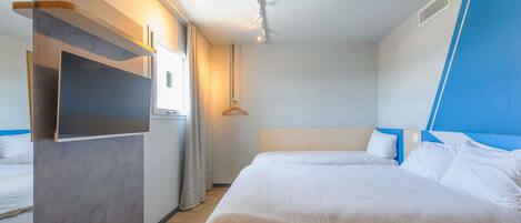 A modern hotel room with a large bed, a built-in TV, and a window with curtains.