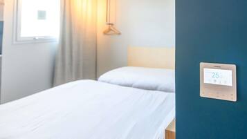 Habitación de hotel con dos camas, una ventana con cortinas, un termostato en la pared y una lámpara colgante.
