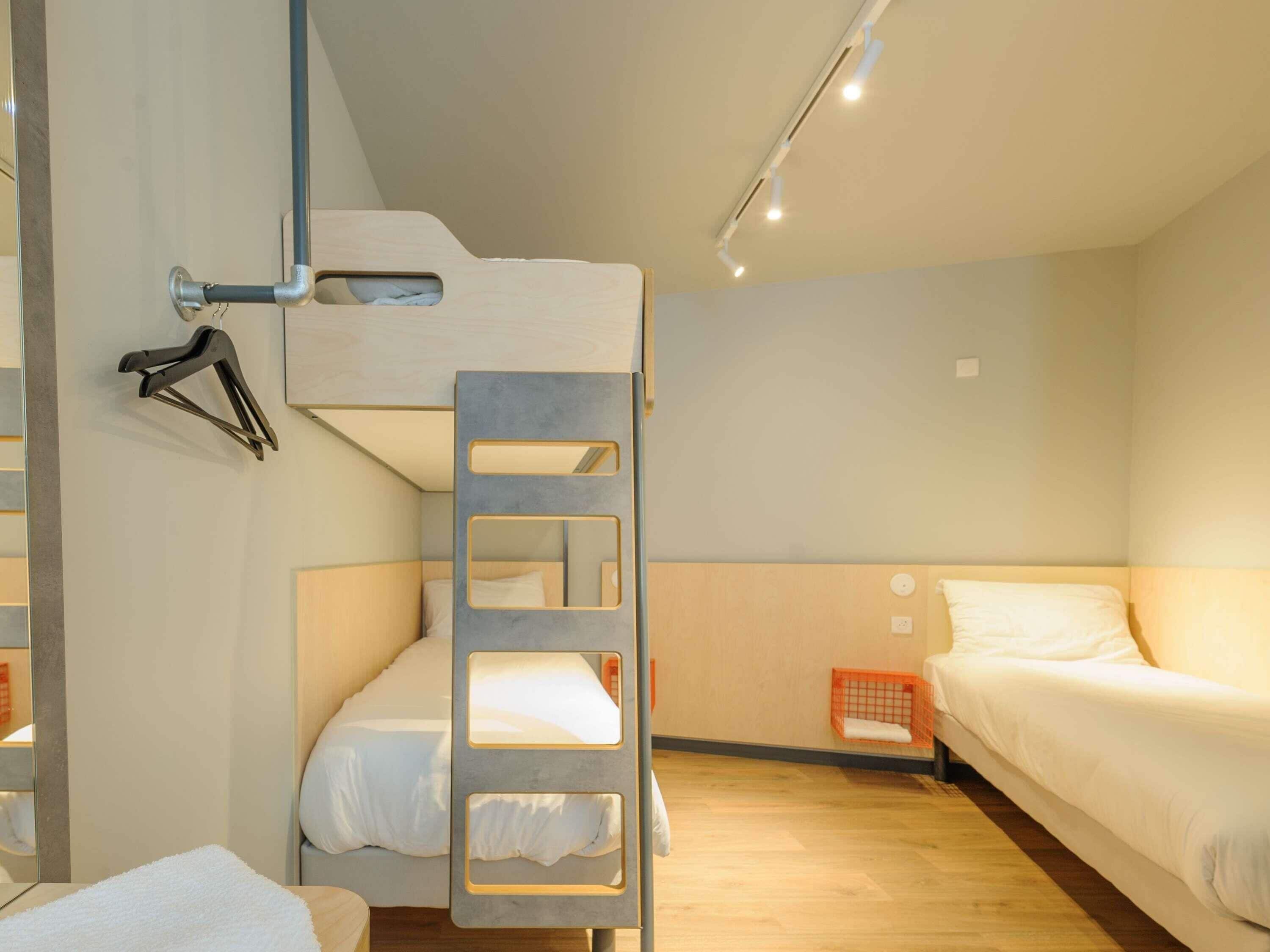 Quarto com beliche, uma pequena cesta de roupa laranja e um porta-toalhas fixado na parede.
