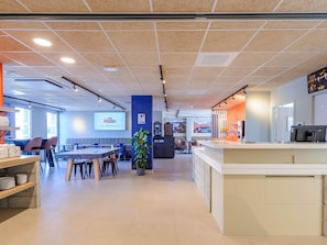 A modern hotel lobby with a reception desk, seating area, and a large screen displaying the hotel name.
