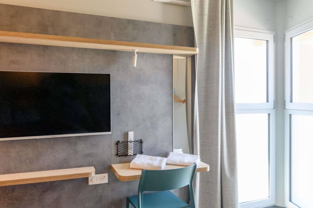 A modern room with a mounted TV, wooden shelves, a chair, and a window with curtains.