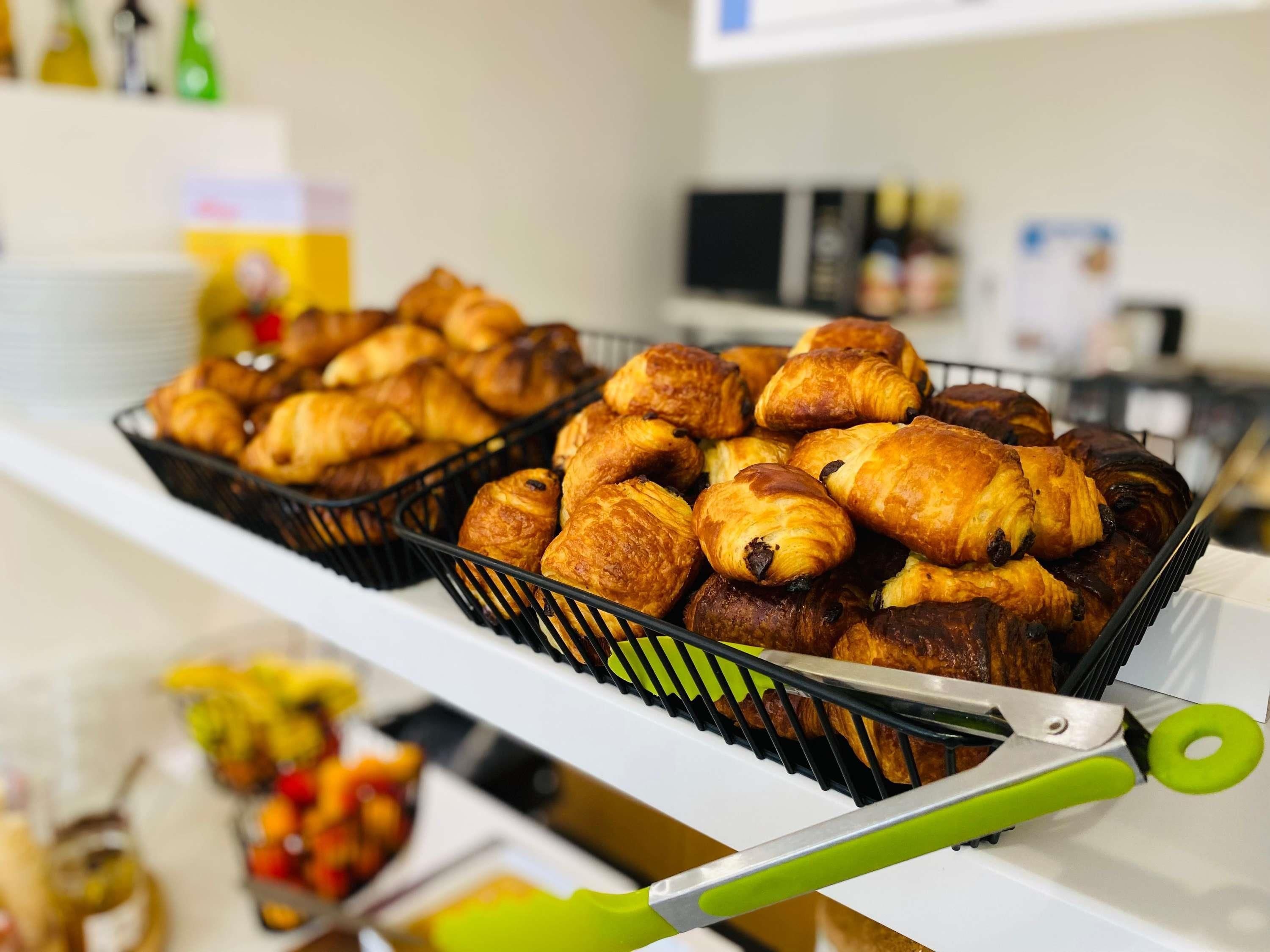 A bakery display with various pastries and a pair of green-handled tongs.