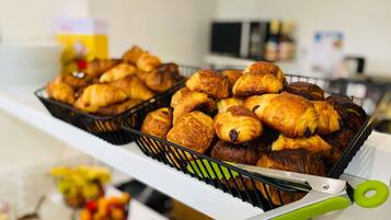A bakery display with various pastries and a pair of green-handled tongs.
