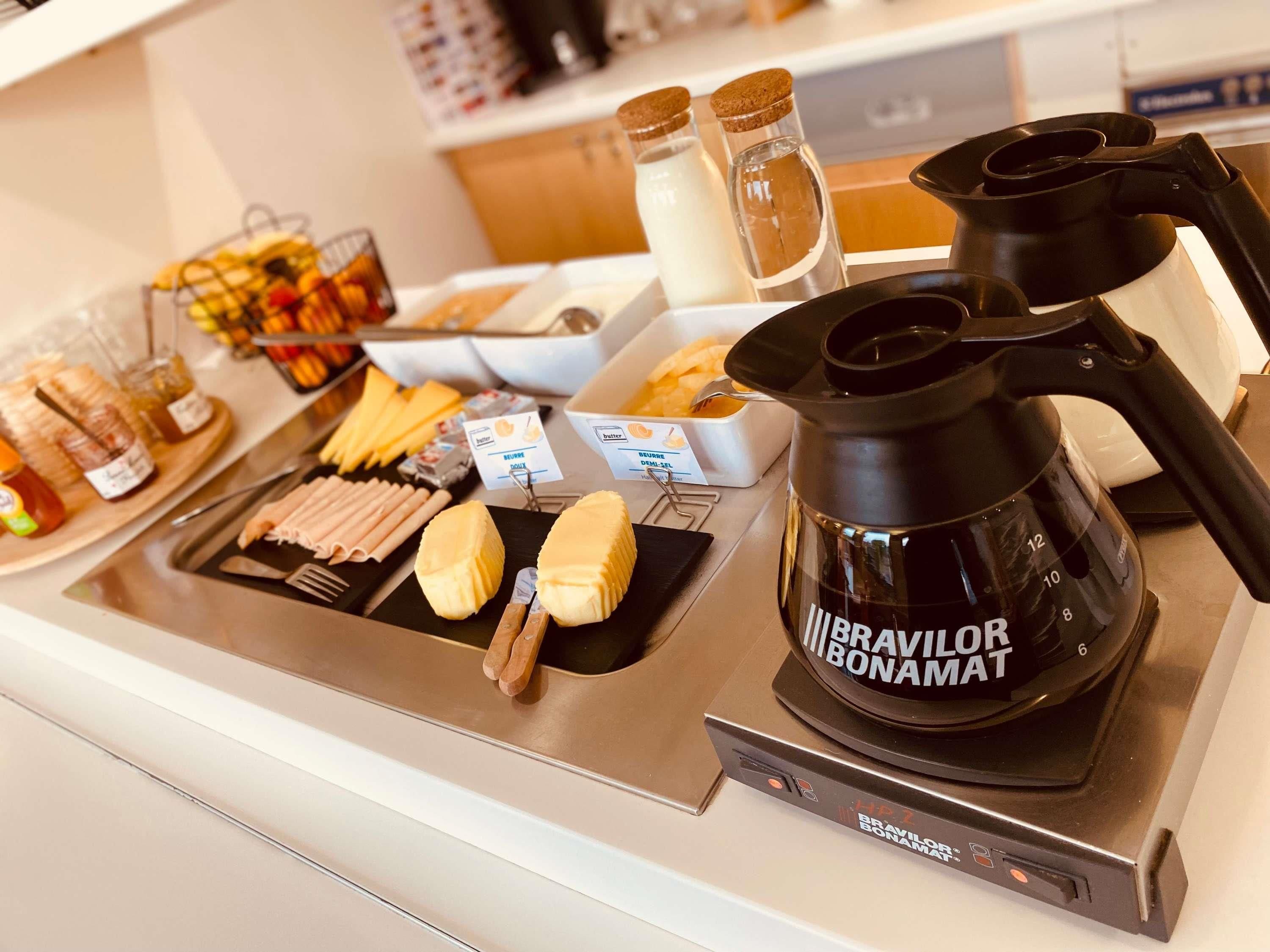 A buffet setup with various food items, a coffee maker, and condiments.