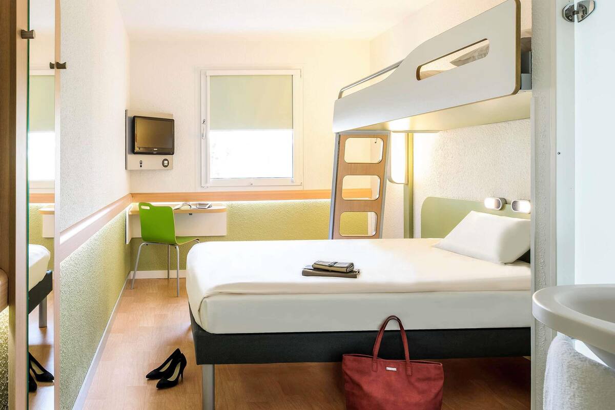 A compact hotel room with a bunk bed, a desk with a chair, a television, and a window.