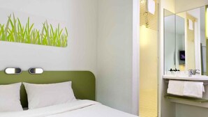 Una habitación de hotel con una cama, un cabecero verde, un espejo en la pared y un baño con lavabo y toallero.