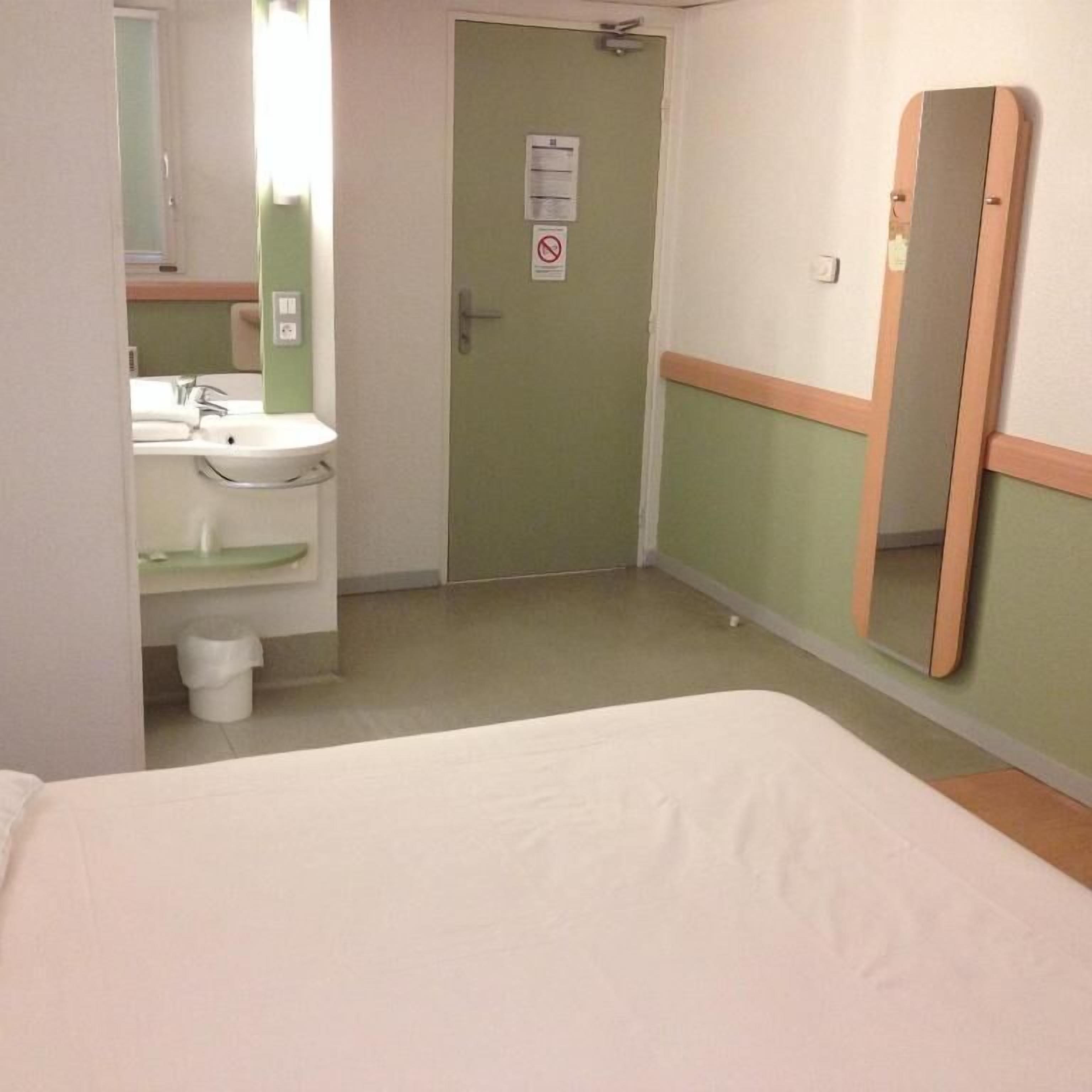 A hotel room with a bed, a sink, and a mirror.