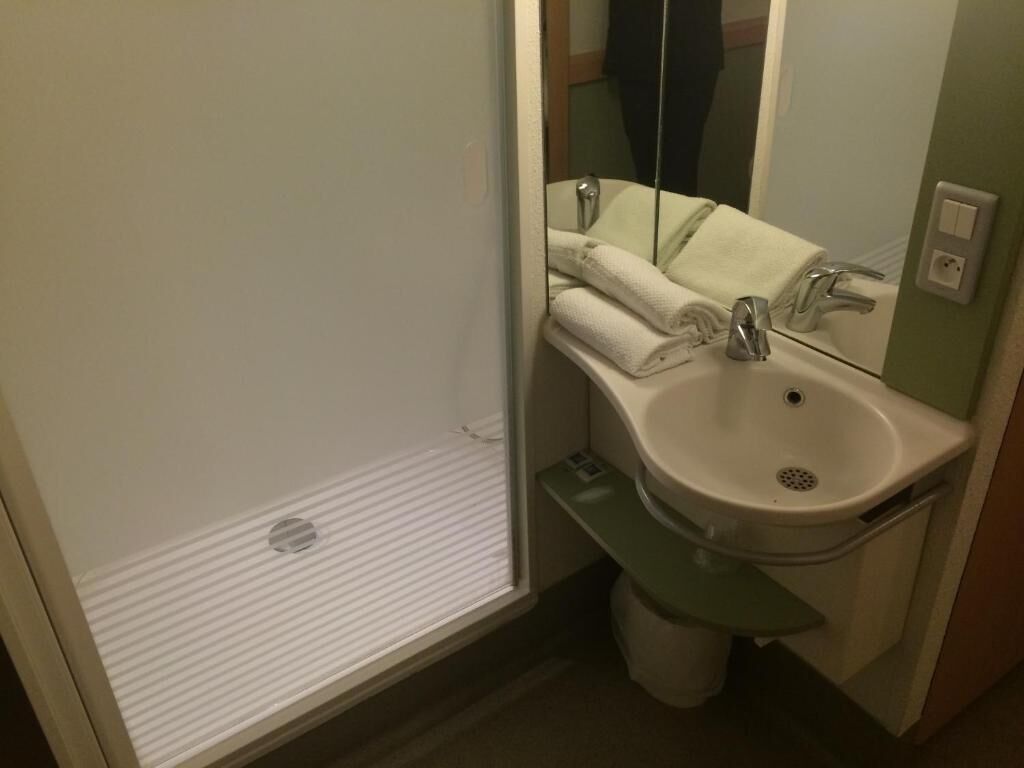 Une salle de bain équipée d’un lavabo, d’un miroir, d’une serviette et d’un espace douche.