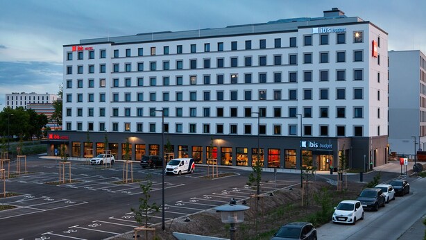 Een modern hotel met meerdere verdiepingen, een parkeerplaats en een nabijgelegen budgetwinkel.