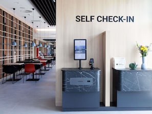 Un espace d’enregistrement autonome comprenant un comptoir d’accueil, un écran d’ordinateur, un terminal de paiement et un panneau indiquant qu’il s’agit d’un espace d’enregistrement autonome.