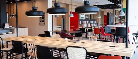 A modern dining area with a long wooden table, black and red chairs, and black pendant lighting.