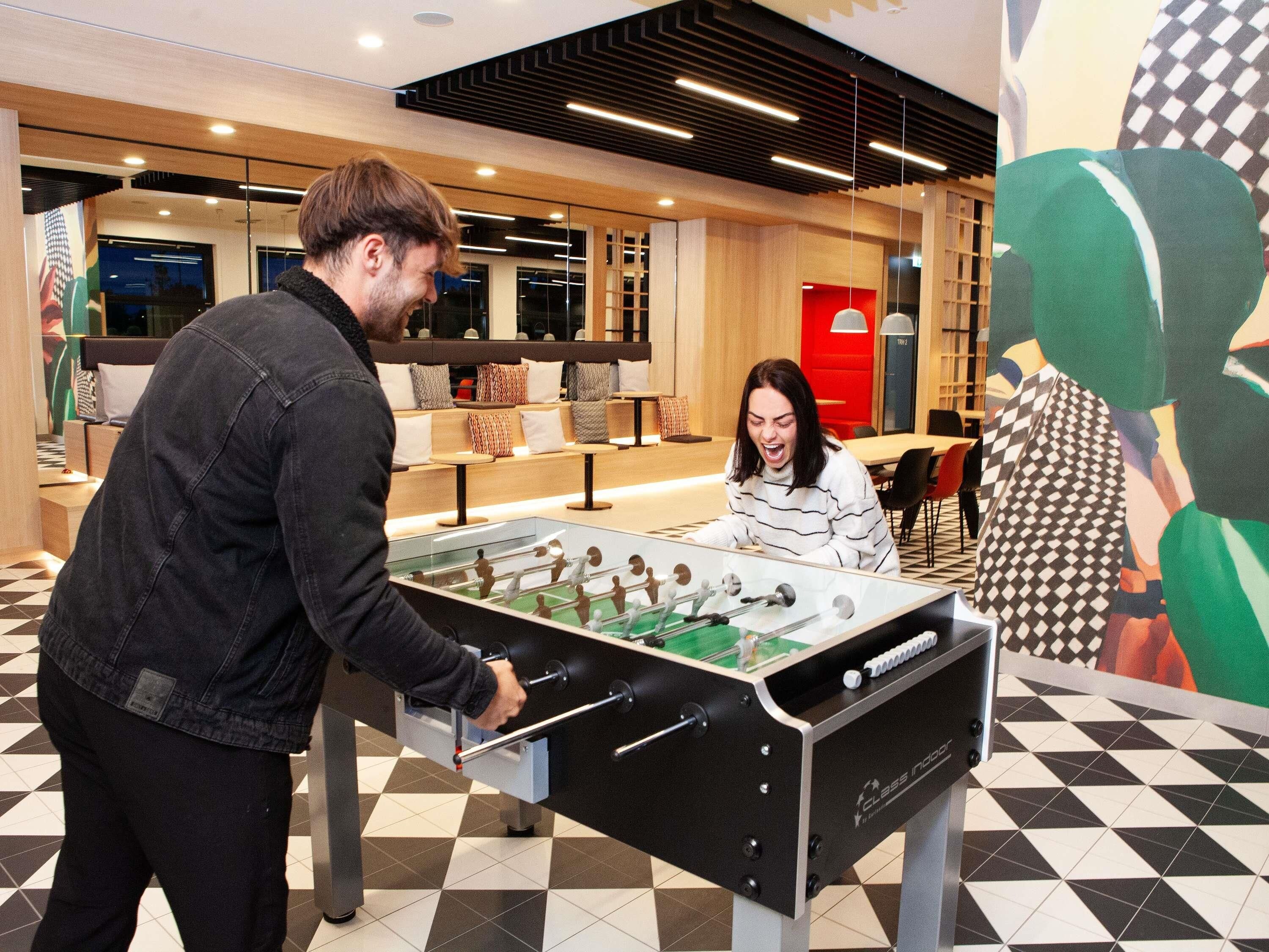 Una mesa de fútbolín en un ambiente interior moderno, con suelo a cuadros y mobiliario contemporáneo.