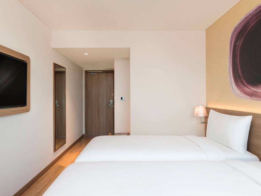 Une chambre d’hôtel avec un grand lit, un téléviseur fixé au mur, un miroir et une porte donnant sur une autre pièce.
