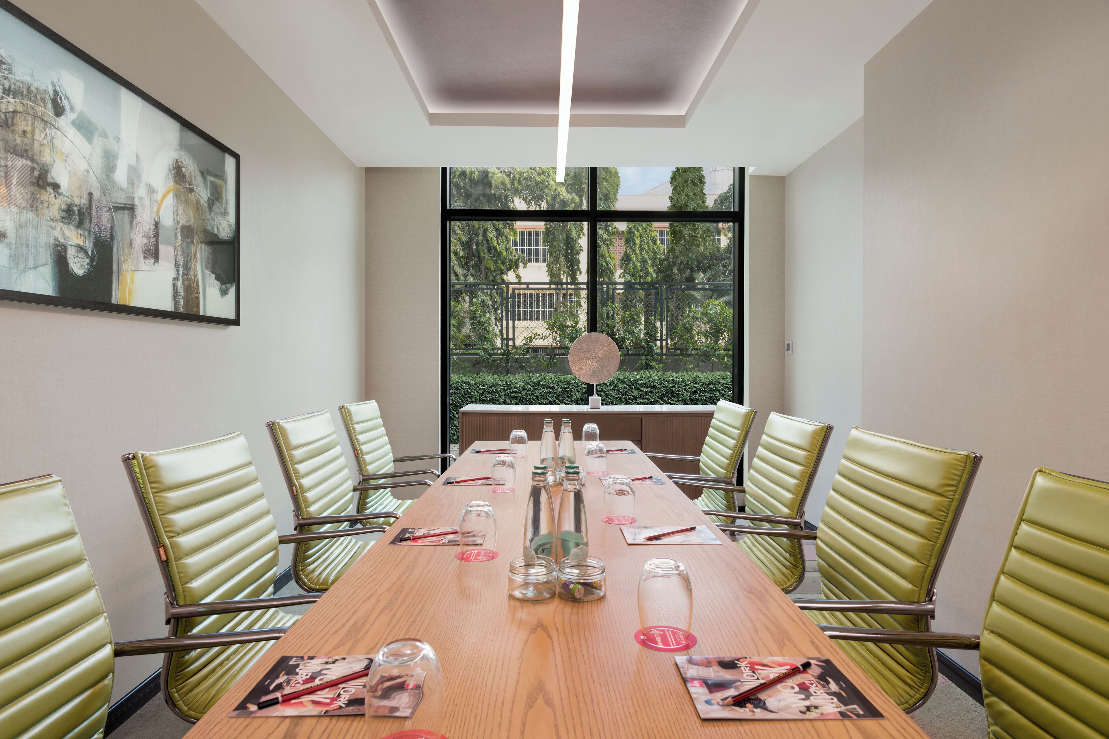 A conference room with a long table, green chairs, and a large window with a view of trees and buildings.