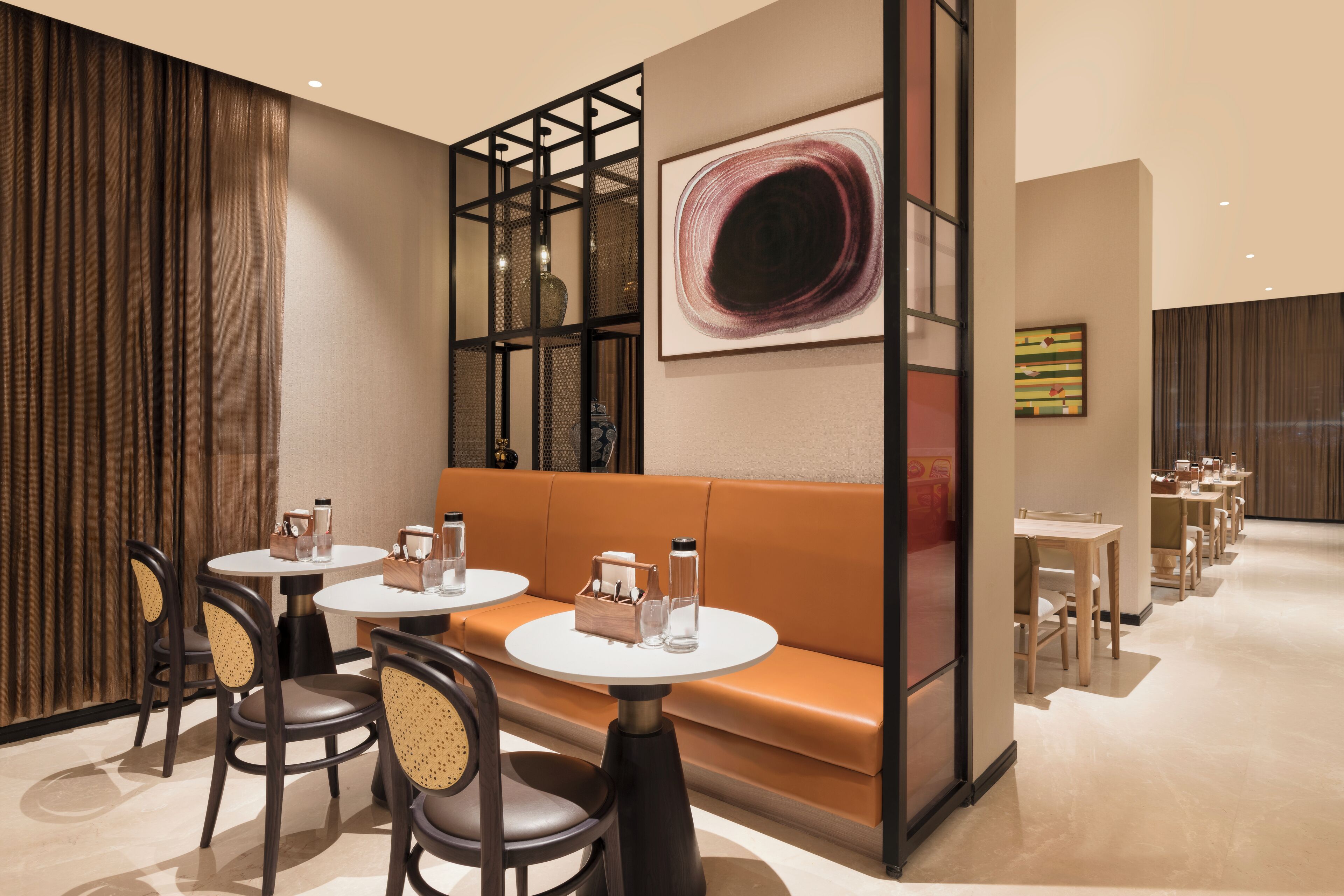 A modern dining area with round tables, cushioned seating, and a decorative wall with artwork.