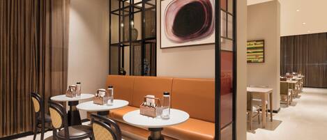 A modern dining area with round tables, cushioned seating, and a decorative wall with artwork.