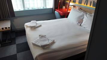 Een hotelkamer met een opgemaakt bed, een bureau en een raam met gordijnen.