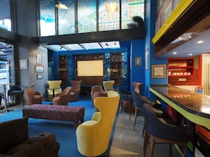Eine Bar mit hoher Decke, blauen Wänden und verschiedenen Sitzgelegenheiten, darunter Stühle und eine Bank.