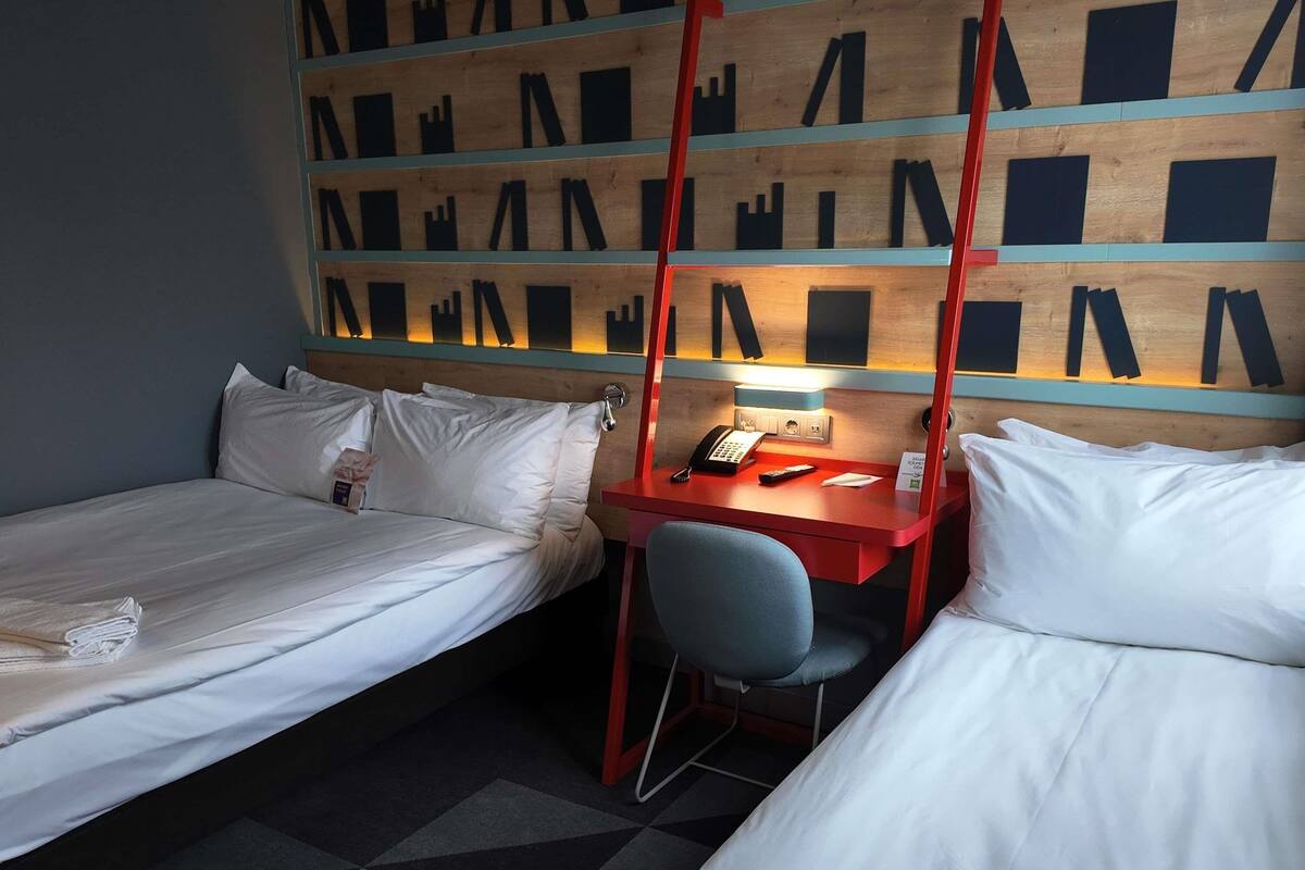 Habitación de hotel con dos camas individuales, un escritorio con silla, un teléfono y una pared con diseños geométricos.