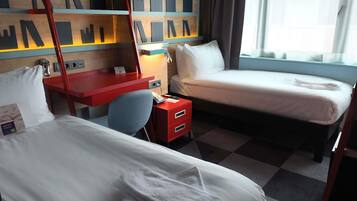 Ein Hotelzimmer mit zwei Betten, einem Schreibtisch, einem Stuhl, einem roten Schrank und einer Wand mit geometrischem Muster.