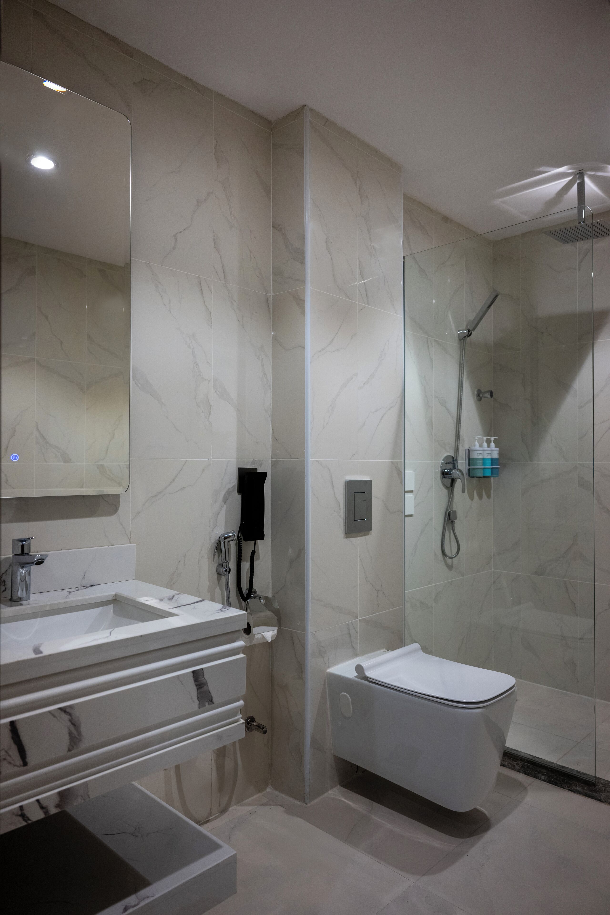 A modern bathroom with a glass-enclosed shower, a white toilet, and a marble-tiled vanity with a double sink.