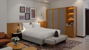 Una habitación de hotel moderna con una cama grande, un armario de madera, una mesita con un florero y un sofá.
