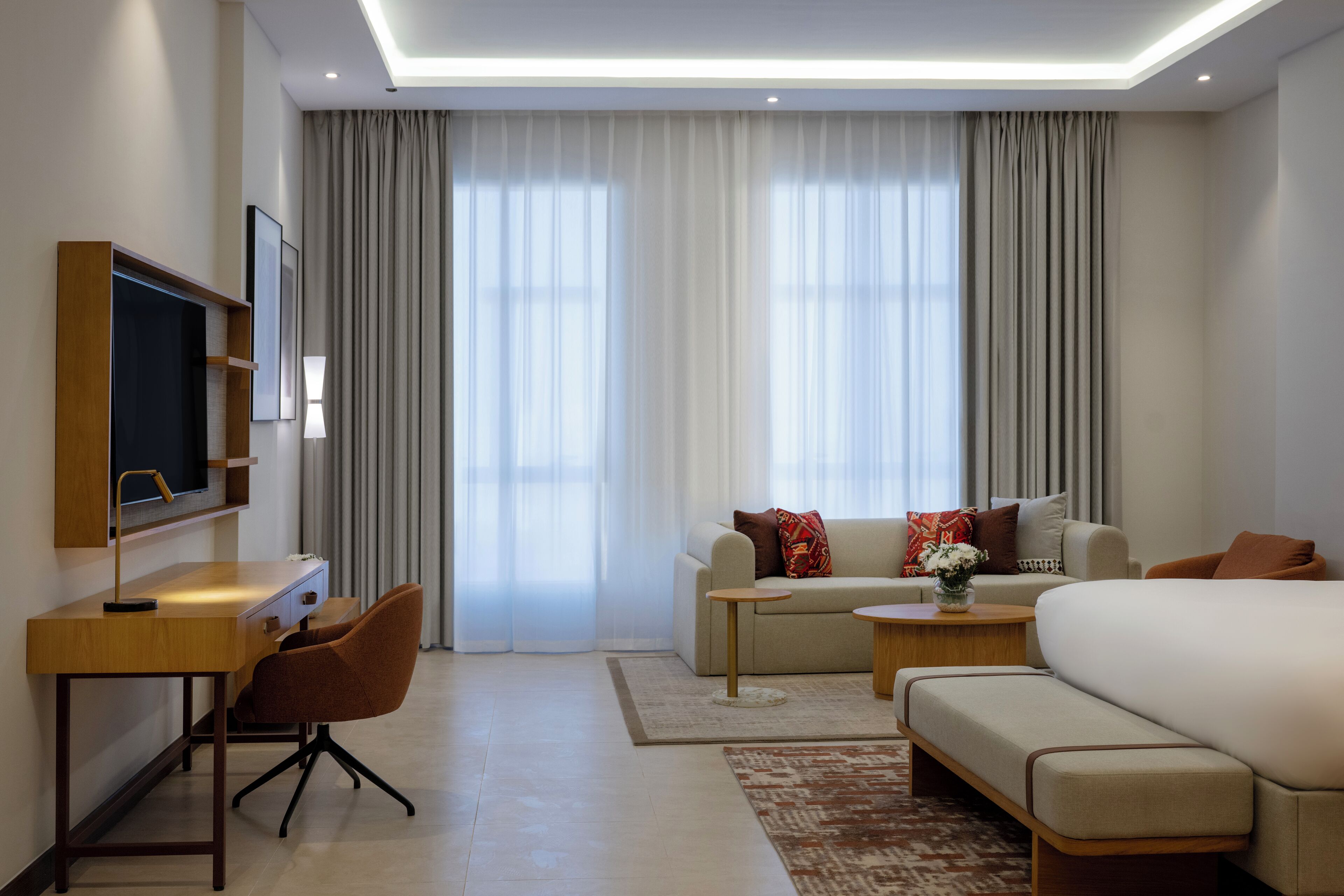 A modern hotel room with a flat-screen TV, a sofa, a bed, a desk, and a coffee table.