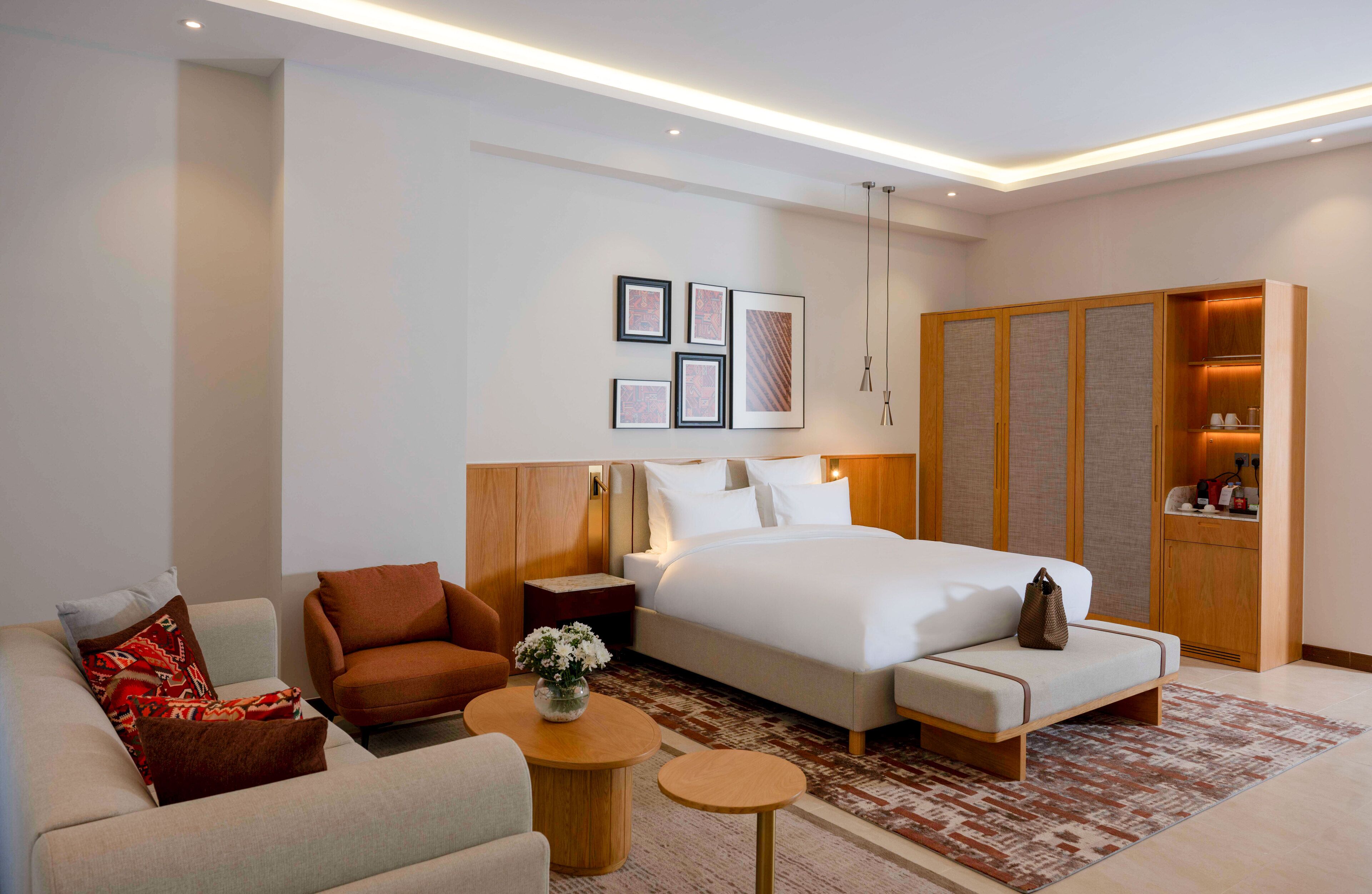 A modern hotel room with a bed, sofa, armchair, and a small table with a vase.