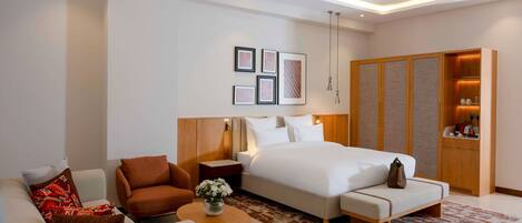 A modern hotel room with a bed, sofa, armchair, and a small table with a vase.
