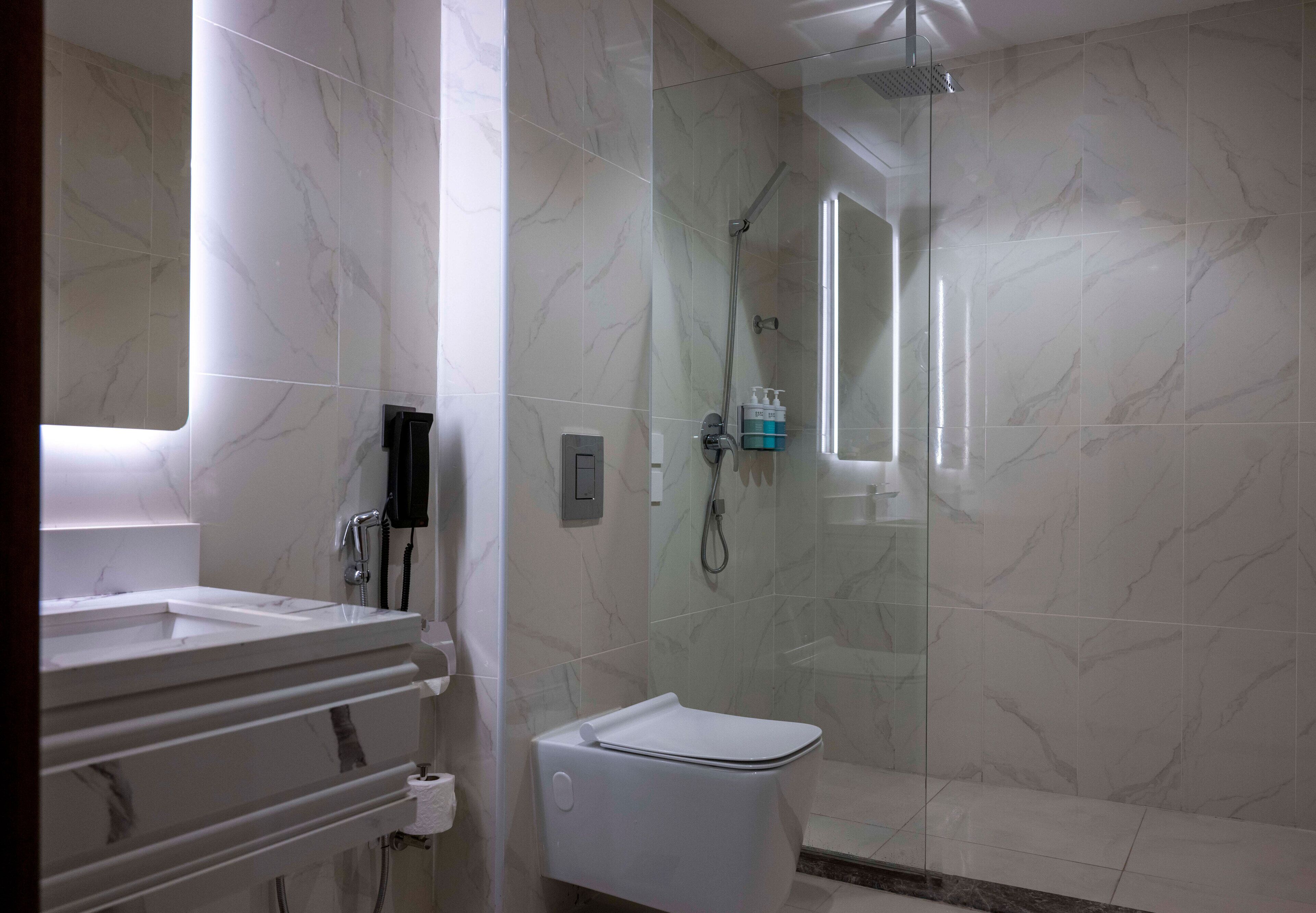 Een badkamer met een douche betegeld met marmer, een wit toilet en een wastafel met een spiegel.