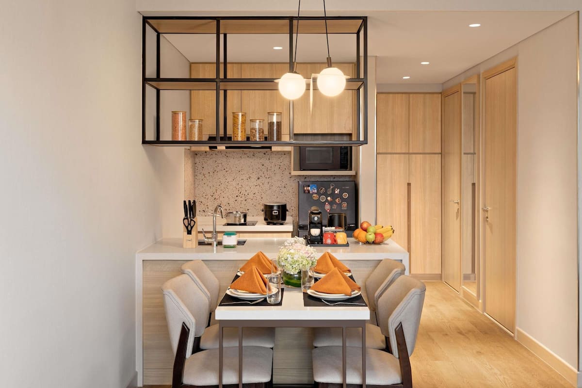 A modern kitchen with a dining area, featuring a central island, overhead lighting, and wooden cabinetry.