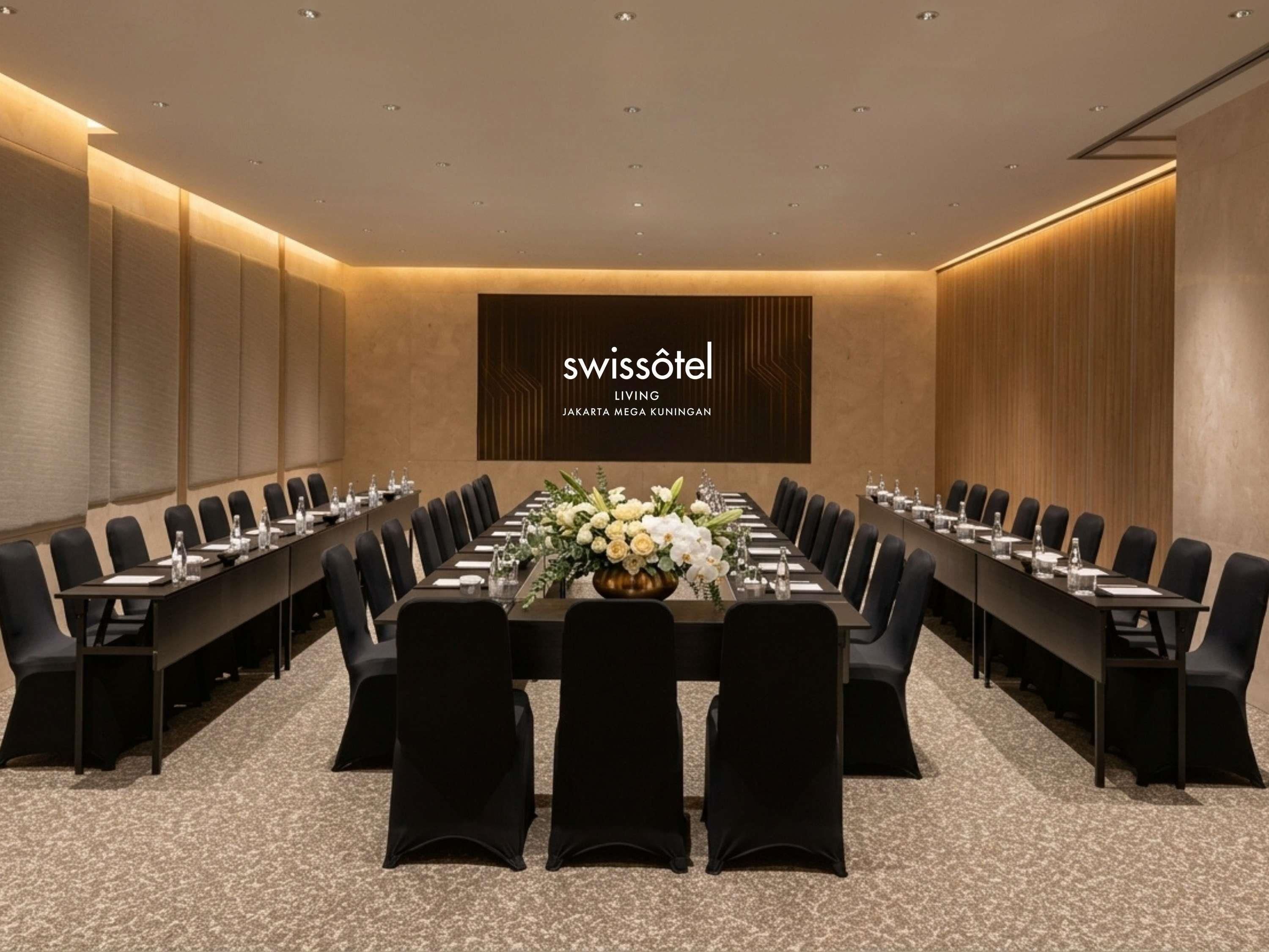 Una sala conferenze con un lungo tavolo, sedie nere e un centrotavola floreale.