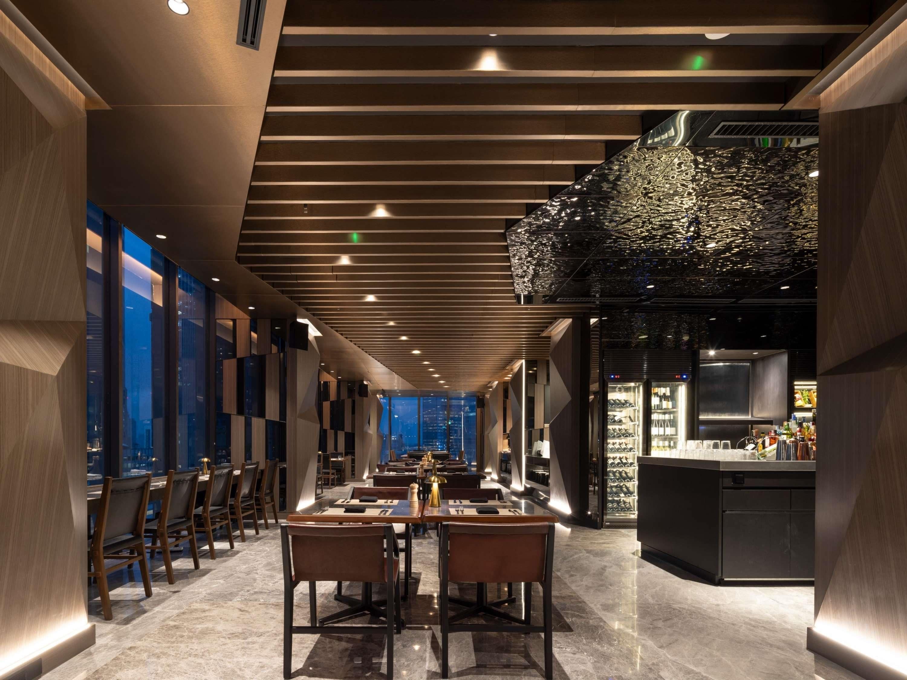 A modern restaurant with a long counter, high ceilings, and a city view.