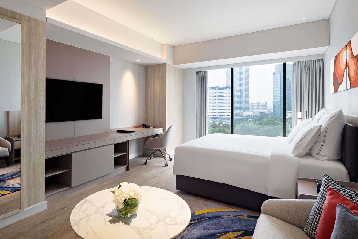 A modern hotel room with a large bed, a flat-screen TV, a desk, and a city view.