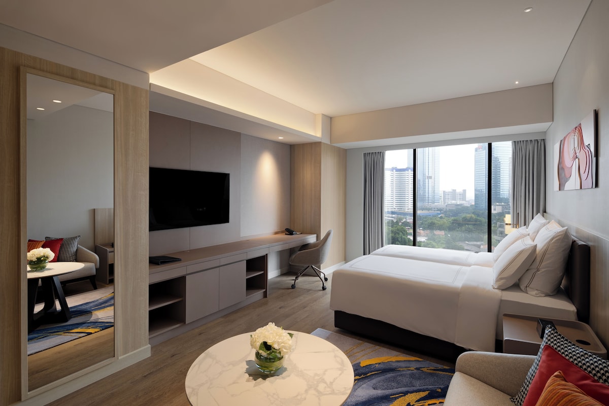 Una habitación de hotel moderna con una cama grande, un escritorio, un televisor y vistas a la ciudad.