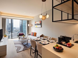 Una habitación de hotel moderna con comedor, sofá, cafetera y vistas a la ciudad.